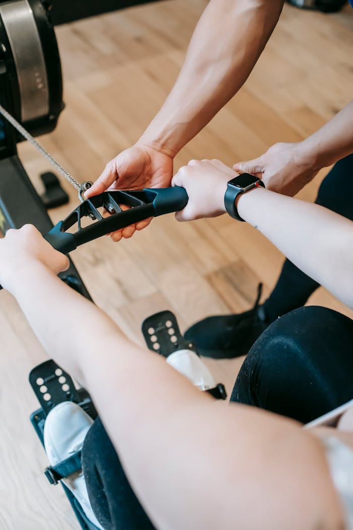 Services-01 Close-up of a personal trainer guiding a client on a rowing machine during a workout session.